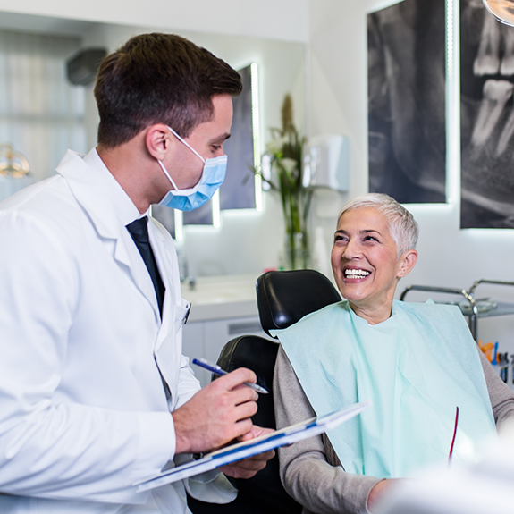 Dentist with mask holding clipboard and talking to patient