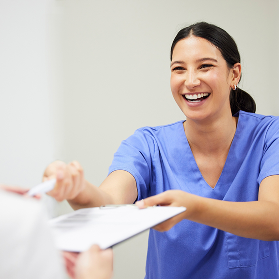 Dentist in blue shirt handing someone a clipboard