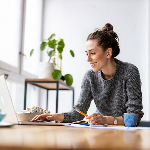 Woman at desk typing on laptop and holding pencil