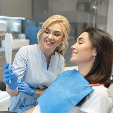 Female dentist holding up mirror for female patient