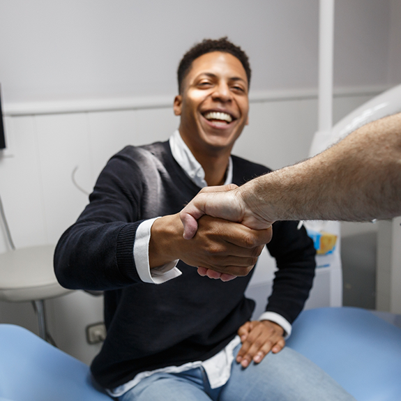 Male patient sitting up in dental chair and shaking dentists hand