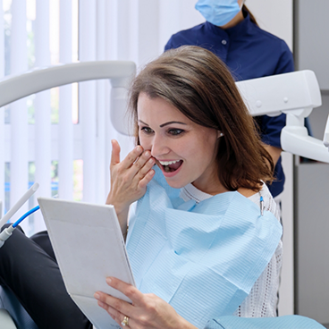 Woman in dental chair checking smile in mirror