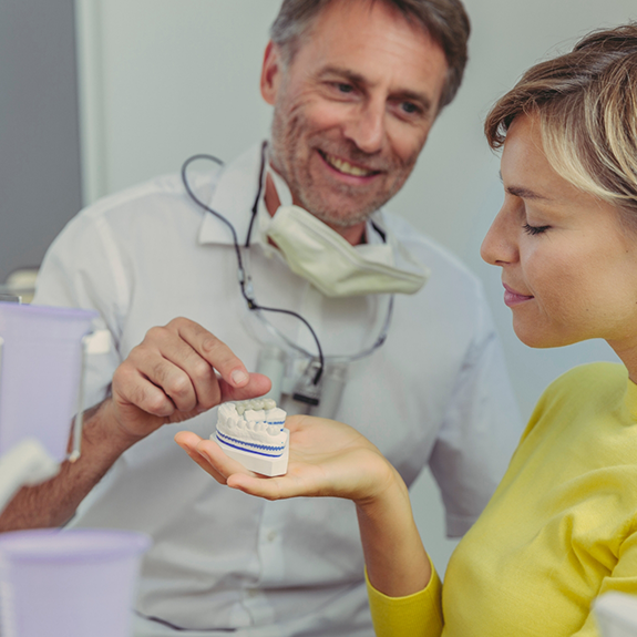 Dentist showing patient model of mouth with dental bridge