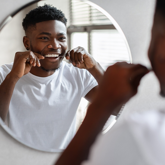 Man looking in mirror flossing his teeth