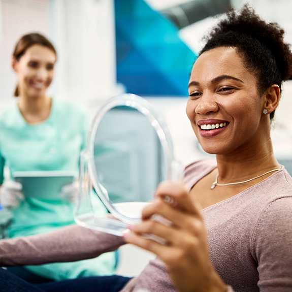 Female dental patient holding up mirror to check smile