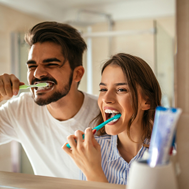 Man and woman brushing teeth in mirror