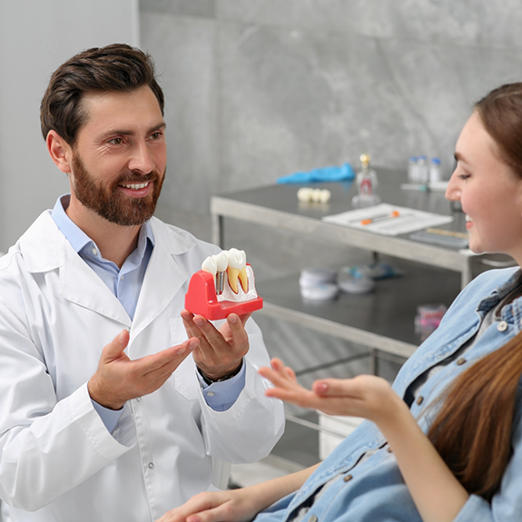 Male dentist showing female patient a dental implant model