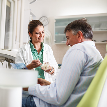 Female dentist showing male patient a dental implant model