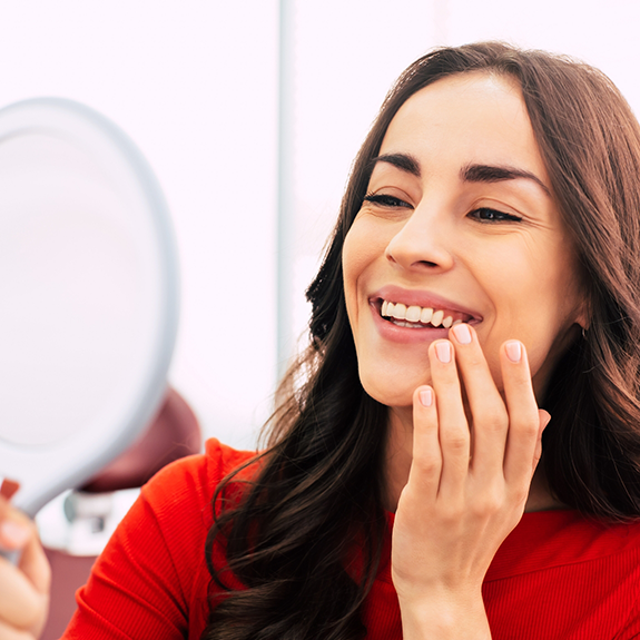 Woman in red shirt checking smile in handheld mirror