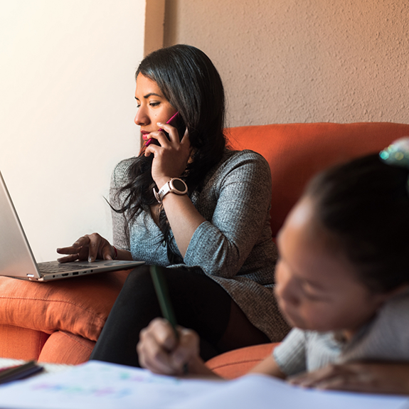 Woman on couch typing on laptop and talking on phone