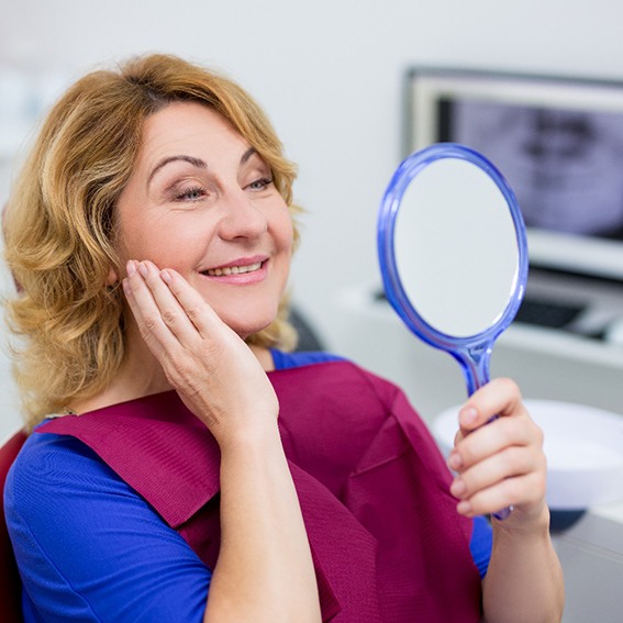 Woman looking at a handheld mirror in dentist’s office smiling