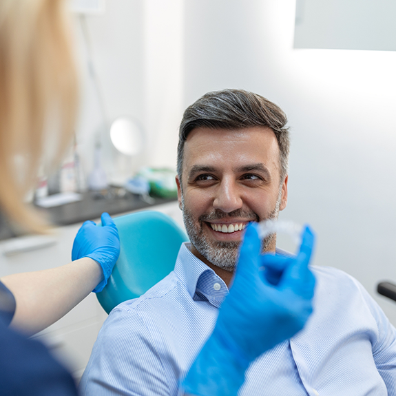 Man sitting in dental chair smiling at dentist holding clear aligner