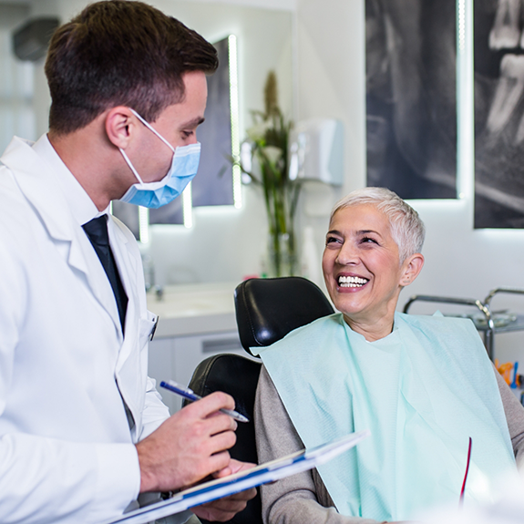 Dentist with mask talking to senior woman in dental chair