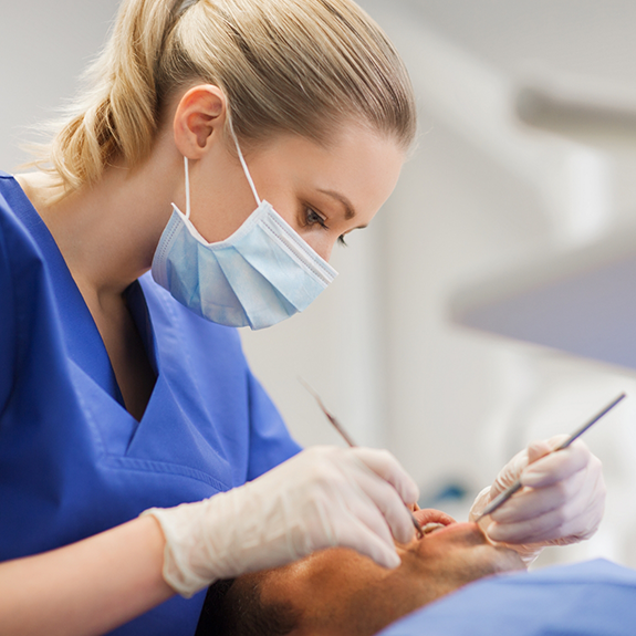 Female dentist with mask examining patients mouth