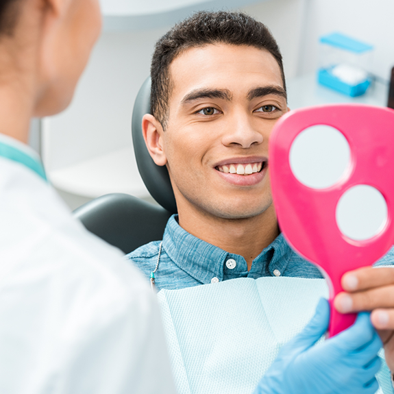 Male dental patient checking smile in mirror held by dentist