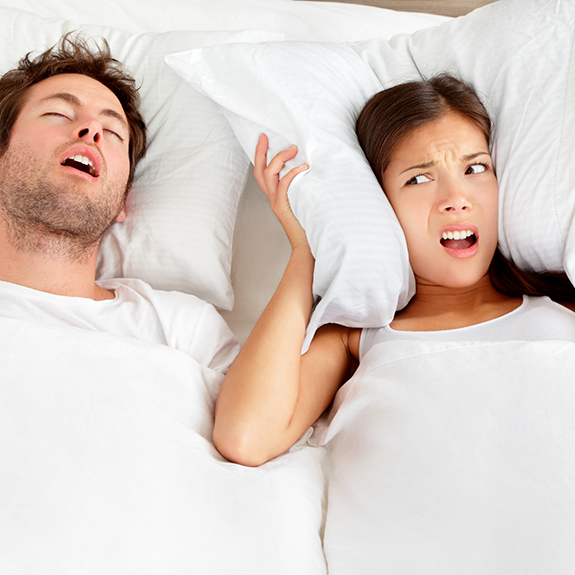 Man snoring and woman covering ears with pillow