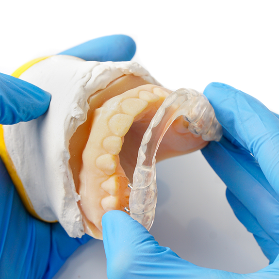 Close up of model of teeth and oral appliance held by gloved hands