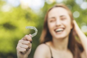 Woman holding aligner, trying to fix TMJ with Invisalign