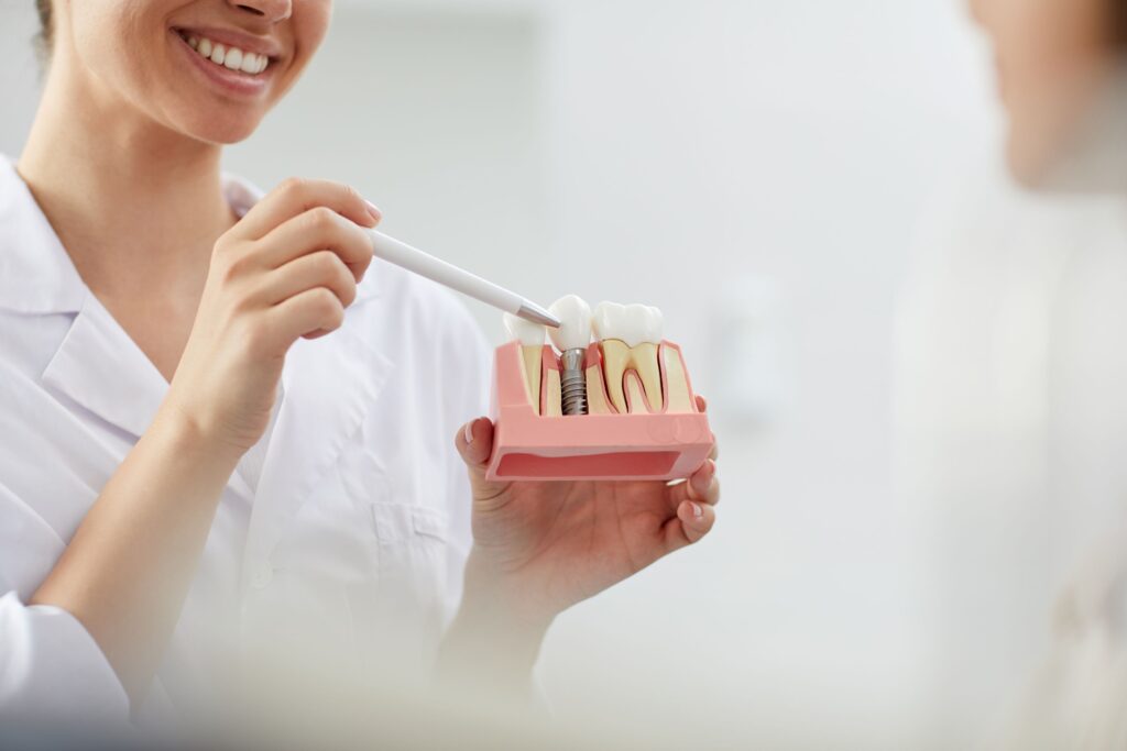 Dentist in white coat pointing to model implant with a white pen