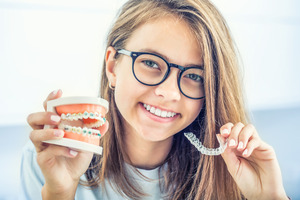 Woman with glasses holding clear aligners and model of teeth with braces